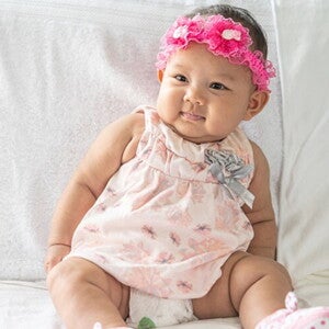 Bebê recém nascida usando vestido florido e laço bordado na cabeça. Bebê recém nascida usando vestido florido e laço bordado na cabeça.