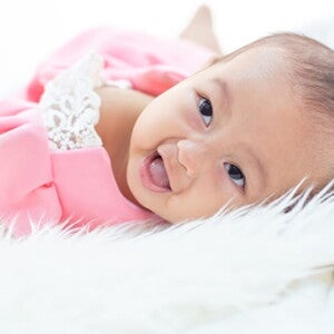 Imagem de bebê recém nascido usando vestido rosa e deitada em uma cama de lençóis brancos. Imagem de bebê recém nascido usando vestido rosa e deitada em uma cama de lençóis brancos.