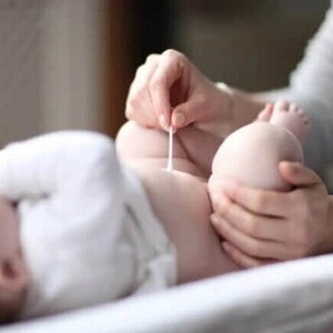 Mamãe limpando o cordão umbilical do bebê com um cotonete.