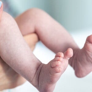 Mãos segurando as perninhas de um recém-nascido avaliando o índice de Apgar Mãos segurando as perninhas de um recém-nascido avaliando o índice de Apgar