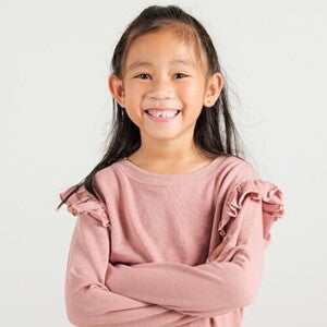 Menina asiática sorrindo com os braços cruzados em frente a uma parede clara Menina asiática sorrindo com os braços cruzados em frente a uma parede clara