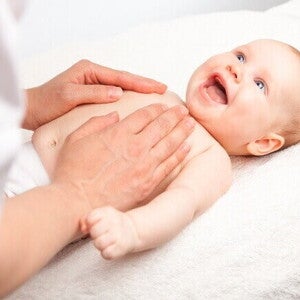 massagem shantala para bebê, com o bebê sorrindo e o adulto aplicando a massagem no peito.