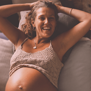 Pregnant woman smiling, with her arms behind her head and top raise to reveal her belly. Pregnant woman smiling, with her arms behind her head and top raise to reveal her belly.