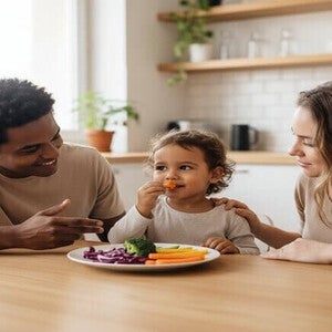 Criança brasileira de 4 anos experimentando novos legumes com os pais na cozinha.