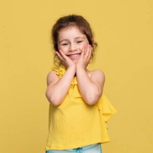 Uma menina sorridente de aproximadamente 3 anos, usando uma blusa amarela, de costas para um fundo amarelo. Uma menina sorridente de aproximadamente 3 anos, usando uma blusa amarela, de costas para um fundo amarelo.