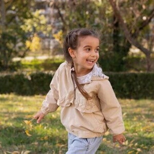 Uma menina de aproximadamente 4 anos brincando ao ar livre em um parque, com um casaco bege e tranças. Uma menina de aproximadamente 4 anos brincando ao ar livre em um parque, com um casaco bege e tranças.