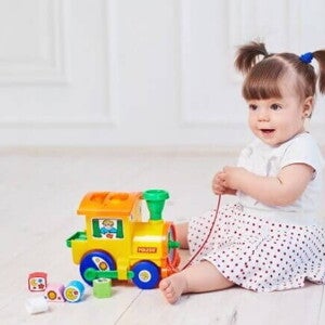 Bebê sentada no chão segurando um trenzinho de brinquedo Bebê sentada no chão segurando um trenzinho de brinquedo