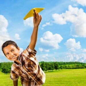 Menino sorridente com aproximadamente 07 anos brincando em um campo verde com um aviãozinho de brinquedo. Menino sorridente com aproximadamente 07 anos brincando em um campo verde com um aviãozinho de brinquedo.