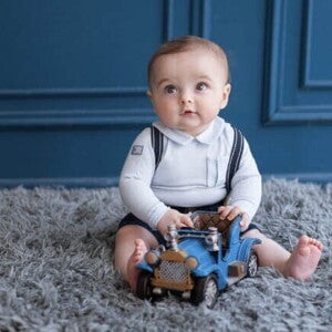 bebê menino sentado em tapete felpudo cinza, com carrinho de brinquedo azul em mãos. bebê menino sentado em tapete felpudo cinza, com carrinho de brinquedo azul em mãos.