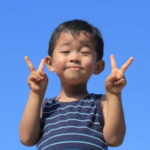Um menino japonês sorrindo, faz um sinal de "V" com as duas mãos, com o céu azul claro ao fundo. Um menino japonês sorrindo, faz um sinal de "V" com as duas mãos, com o céu azul claro ao fundo.