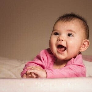 Bebê sorridente deitada de bruços na cama usando uma roupa cor de rosa. Bebê sorridente deitada de bruços na cama usando uma roupa cor de rosa.