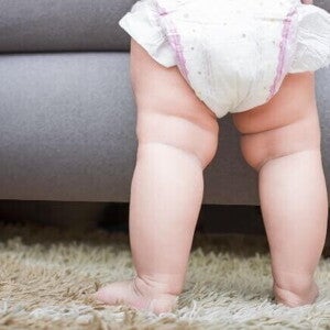 Imagem das pernas de um bebê em pé, em cima de um tapete Imagem das pernas de um bebê em pé, em cima de um tapete