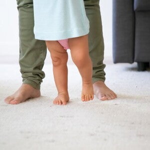 pai, usando calça verde, ajudando o filho a dar os primeiros passos pai, usando calça verde, ajudando o filho a dar os primeiros passos