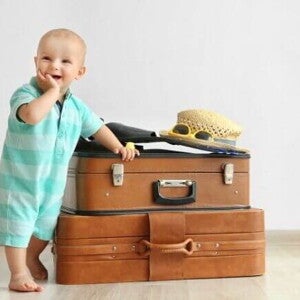 Bebê sorrindo, com a mão na boca, apoiado em malas de viagem. Bebê sorrindo, com a mão na boca, apoiado em malas de viagem.