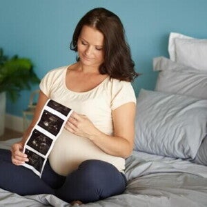Mulher grávida sentada em uma cama, observando o resultado de um exame de ultrassom Mulher grávida sentada em uma cama, observando o resultado de um exame de ultrassom