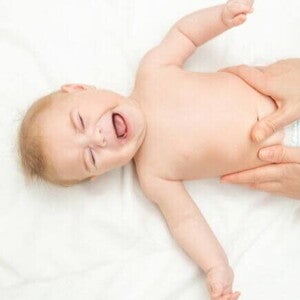 Bebê deitado de costas em uma superfície branca, chorando, enquanto um adulto realiza uma massagem suave em sua barriga. Bebê deitado de costas em uma superfície branca, chorando, enquanto um adulto realiza uma massagem suave em sua barriga.