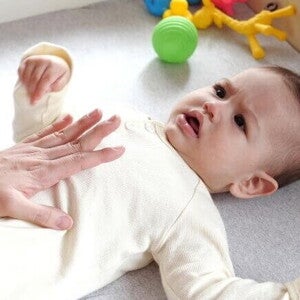 Mão de um adulto massageando suavemente a barriga de um bebê deitado, que parece estar com cólica ou outro desconforto.