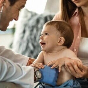 Menino sorridente de aproximadamente um ano sentado no colo da mãe recebendo atendimento médico Menino sorridente de aproximadamente um ano sentado no colo da mãe recebendo atendimento médico