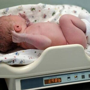 Um recém-nascido é pesado em uma balança hospitalar, com o visor mostrando 3.986 kg, ilustrando a medição para determinar qual o peso normal de um recém-nascido.