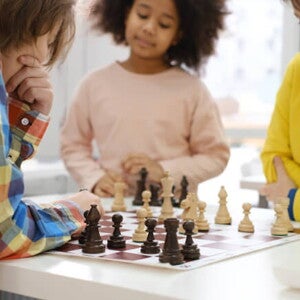 três crianças ao redor de mesa jogando xadrez três crianças ao redor de mesa jogando xadrez