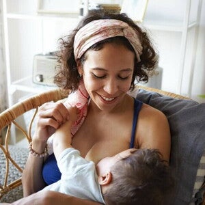 Mãe sentada e sorrindo, amamentando um bebê em seu colo
