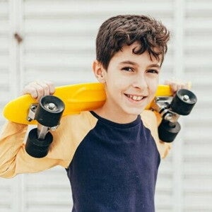 Menino sorrindo e segurando um skate pequeno em cima dos ombros Menino sorrindo e segurando um skate pequeno em cima dos ombros