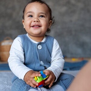 Bebê de aproximadamente 1 ano sentado no tapete da sala segurando brinquedos. Bebê de aproximadamente 1 ano sentado no tapete da sala segurando brinquedos.
