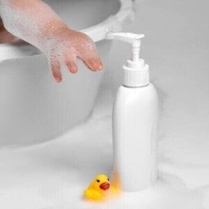 Mão de um bebê se esticando para alcançar um frasco de shampoo ao lado de um pato de borracha. Mão de um bebê se esticando para alcançar um frasco de shampoo ao lado de um pato de borracha.