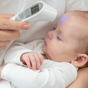 Uma mão medindo a temperatura do bebê com termômetro digital na testa. Uma mão medindo a temperatura do bebê com termômetro digital na testa.