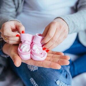 mulher grávida segura um par de sapatinhos rosas de bebê 
