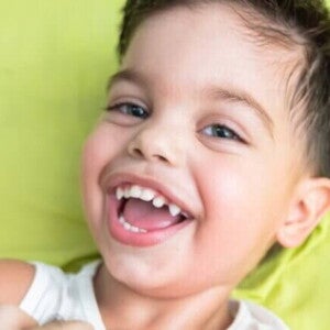 Menino em cima da cama com roupa branca sorrindo Menino em cima da cama com roupa branca sorrindo