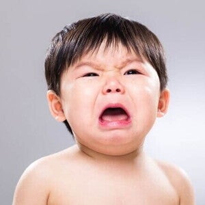 Bebê chorando com expressão intensa de angústia, boca aberta e olhos fechados parcialmente, em um fundo neutro cinza. Bebê chorando com expressão intensa de angústia, boca aberta e olhos fechados parcialmente, em um fundo neutro cinza.