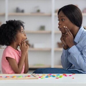 Uma menina e uma mulher sentadas frente a frente, com os dedos sobre as bochechas e as bocas abertas Uma menina e uma mulher sentadas frente a frente, com os dedos sobre as bochechas e as bocas abertas