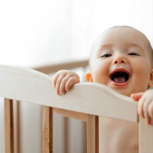 Bebê de 6 meses parado em seu berço se segurando na grade. [