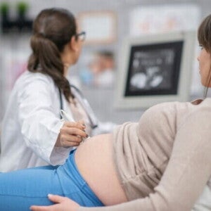 Uma mulher grávida deitada enquanto uma profissional de saúde realiza um ultrassom abdominal.