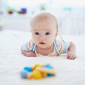 Um bebê deitado de barriga para baixo na cama, praticando tummy time, enquanto veste um body colorido. Um bebê deitado de barriga para baixo na cama, praticando tummy time, enquanto veste um body colorido.
