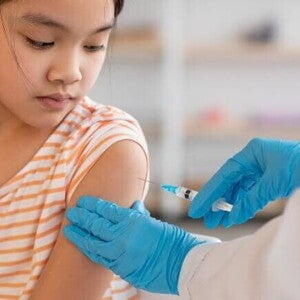 Uma criança recebendo uma injeção no braço de um profissional de saúde usando luvas azuis, simbolizando a aplicação da vacina HPV.