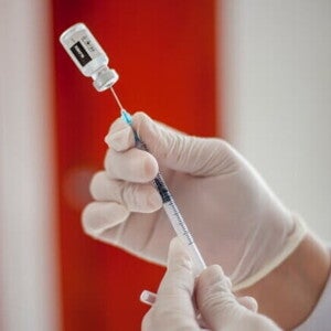 Profissional de saúde com luvas preparando uma seringa com uma dose de vacina retirada de um frasco.