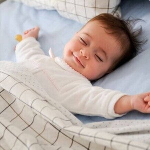 Bebê dormindo de barriga para cima em uma cama com lençóis e cobertor, transmitindo sensação de conforto e tranquilidade. Bebê dormindo de barriga para cima em uma cama com lençóis e cobertor, transmitindo sensação de conforto e tranquilidade.