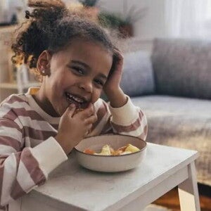 Foto de uma criança fazendo um lanche e comendo com as mãos uma vasilha de salada de frutas, um exemplo de alimento rico em vitamina C Foto de uma criança fazendo um lanche e comendo com as mãos uma vasilha de salada de frutas, um exemplo de alimento rico em vitamina C