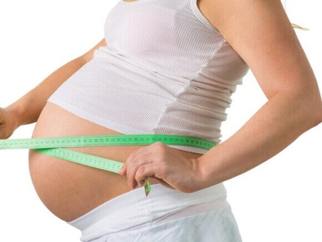 Mulher grávida de 33 semanas de gravidez medindo a circunferência da barriga com fita métrica, um marco no terceiro trimestre.