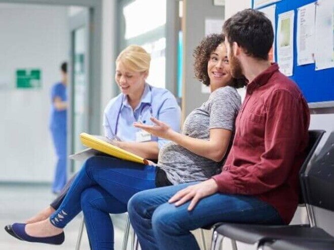 Gestante conversando com médico e acompanhante em hospital
