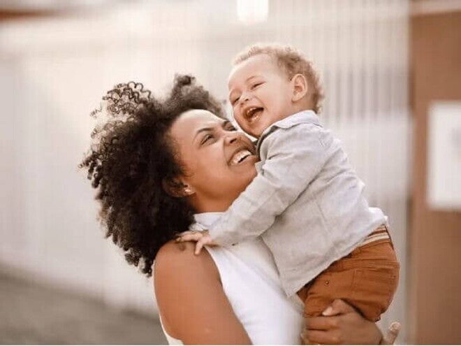 Mãe sorridente carrega o filho no colo, ilustrando a fase conhecida como terrible two. Mãe sorridente carrega o filho no colo, ilustrando a fase conhecida como terrible two.
