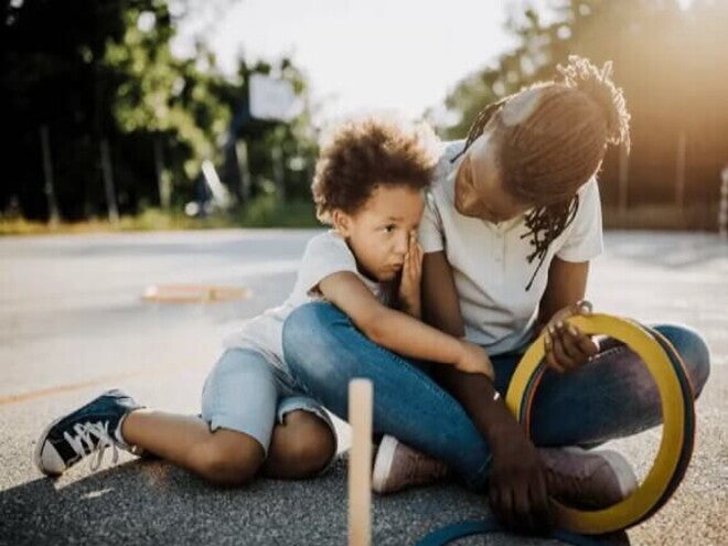Mãe e filho, uma criança de 6 anos, estão sentados no chão de um espaço ao ar livre. A mãe olha para o filho, que o abraça. Mãe e filho, uma criança de 6 anos, estão sentados no chão de um espaço ao ar livre. A mãe olha para o filho, que o abraça.