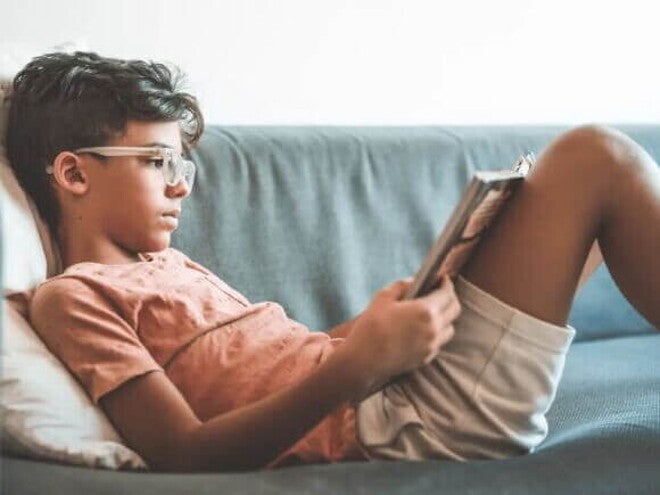 Criança de 7 anos lendo um livro deitada em um sofá, apoiada em uma almofada. Criança de 7 anos lendo um livro deitada em um sofá, apoiada em uma almofada.