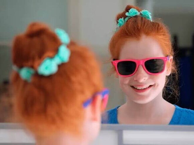 Menina sorri para a própria imagem no espelho. Se trata de uma criança de cerca de 9 anos usando óculos escuros com armação rosa. Menina sorri para a própria imagem no espelho. Se trata de uma criança de cerca de 9 anos usando óculos escuros com armação rosa.