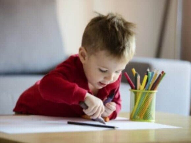Criança pequena colorindo uma folha branca, aprendendo cores.