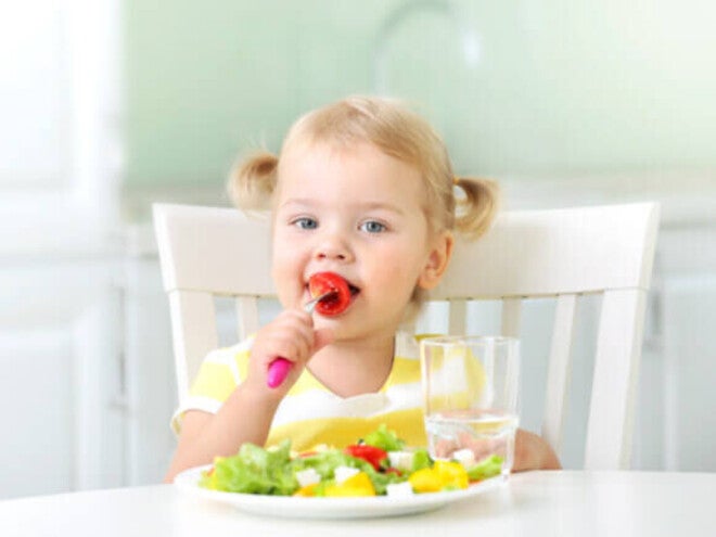 Pequeña comiendo verduras durante la comida.