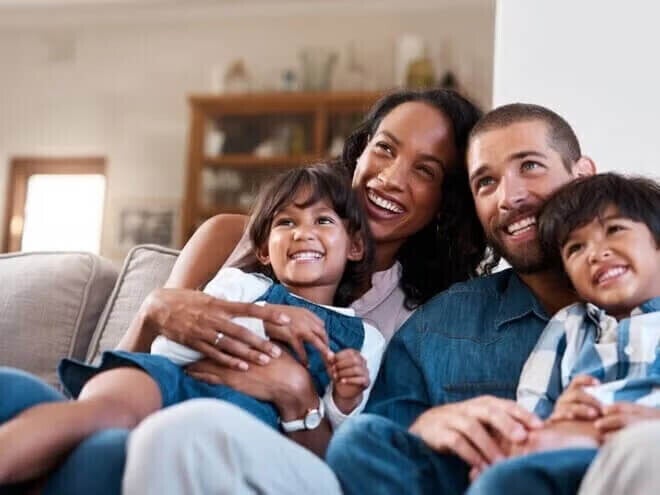 Família com dois filhos em idade escolar assistindo TV juntos em casa.