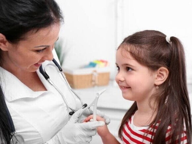 Menina com a boca aberta sendo examinada por um médico, simulando a avaliação de problemas respiratórios e de garganta relacionados à adenoide.